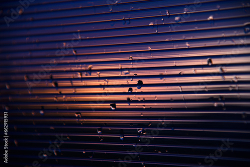 Blue-purple polycarbonate with raindrops. View of wet glass in the setting sun.