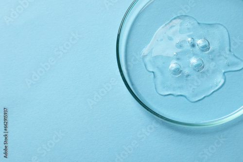 Petri dish with sample of cosmetic oil on light blue background, above view. Space for text