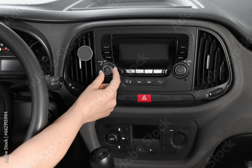 Listening to radio while driving. Woman turning volume button on vehicle audio in car, closeup