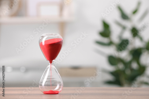 Hourglass with red flowing sand on table against blurred background. Space for text