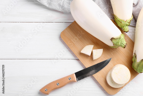 Board, raw white eggplants and knife on wooden table, flat lay. Space for text
