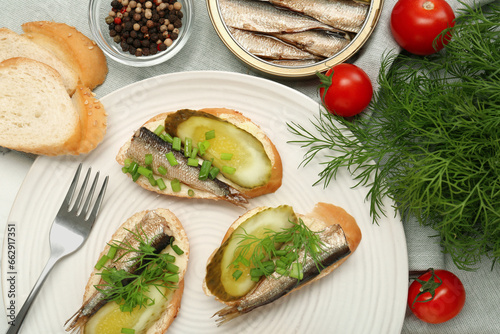Delicious sandwiches with sprats, pickled cucumber, green onion and dill served on table, flat lay