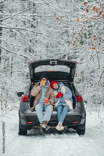 A couple in a snowy forest stopped for a drink and snack and a rest from the road