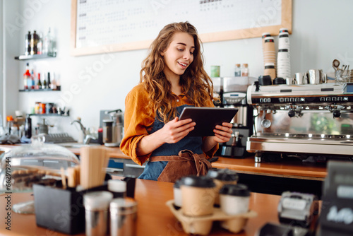 Female barista takes an order from a tablet while standing behind the counter in a coffee shop. Business, technology concept. Takeaway food.