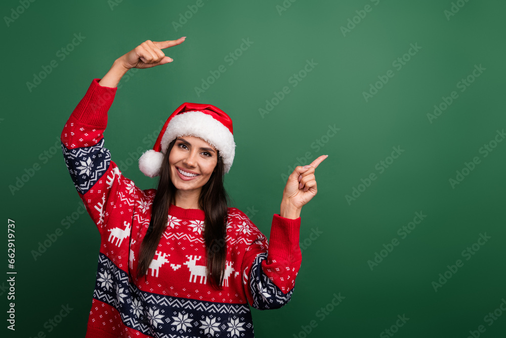 Photo of cute cheerful woman santa elf wear ornament x-mas pullover pointing two fingers empty space isolated green color background