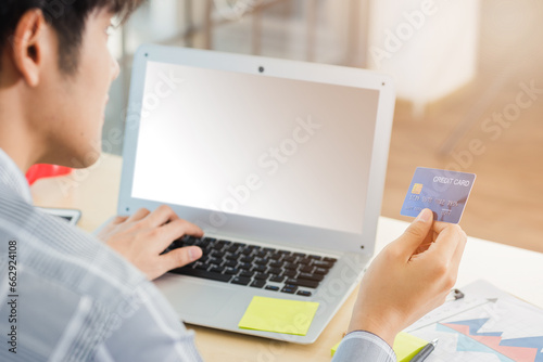 Asian business man hand holding credit card and typing entering security code on a laptop computer for process payment online shopping on the internet at the home office