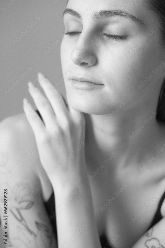 Black and white portrait of a brunette girl without make up on a grey backgroung in a black summer clothes. Woman is sitting on a chair Black and white portrait of a brunette girl without make up on a grey backgroung in a black summer clothes. Woman is sitting on a chair