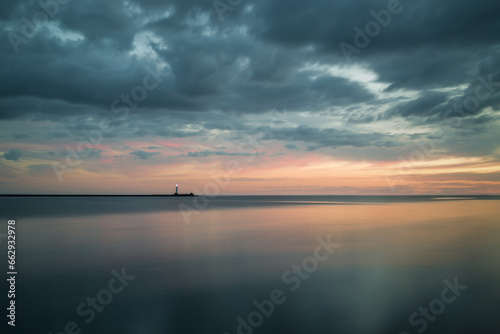 Long exposure image of dramatic sky seascape with rock in sunset scenery background