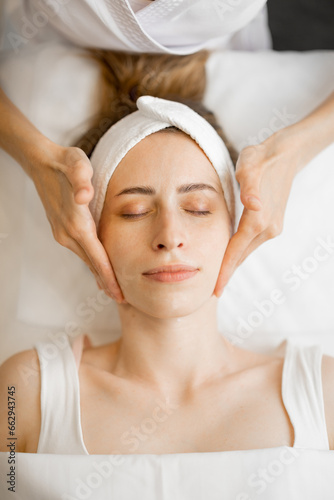 Beautician makes professional face massage for the woman's face at beauty salon. Young adult caucasian woman receiving relaxing facial massage