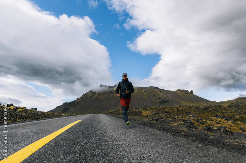 A fast runner is running in a wasteland in Iceland on the road.