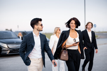 Group of an elegant business people talk on the go on parking lot, arrived by business class taxis. Concept of vehicle transfer and business travel