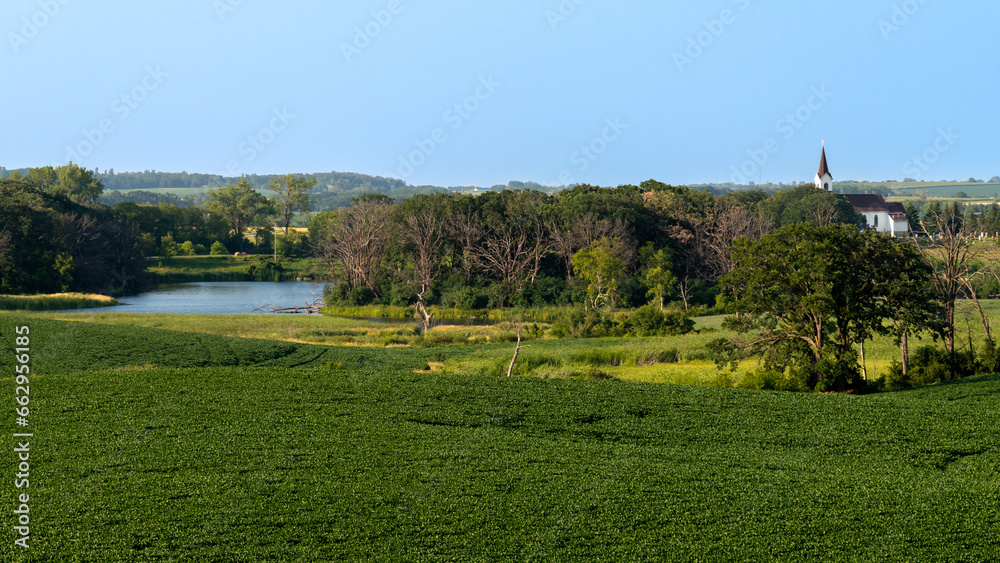 Panoramic view of the countryside with different crops in the fields, a lake and a white church in rural west central Minnesota, United States.
