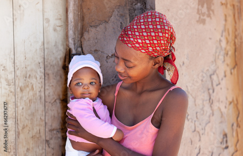 young african mother in the village holding her baby in front of the house