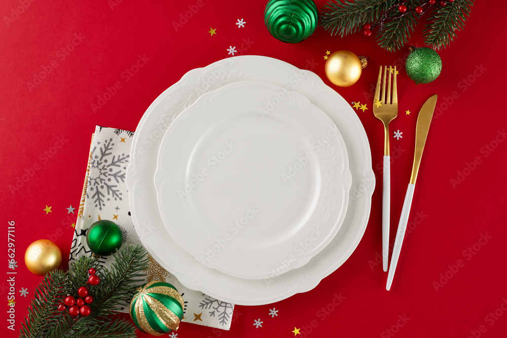 Elevate your feast: the Christmas table preparation. Top view composition of gold cutlery, plates, napkin, fir twigs, holiday baubles, stars confetti on red background Elevate your feast: the Christmas table preparation. Top view composition of gold cutlery, plates, napkin, fir twigs, holiday baubles, stars confetti on red background