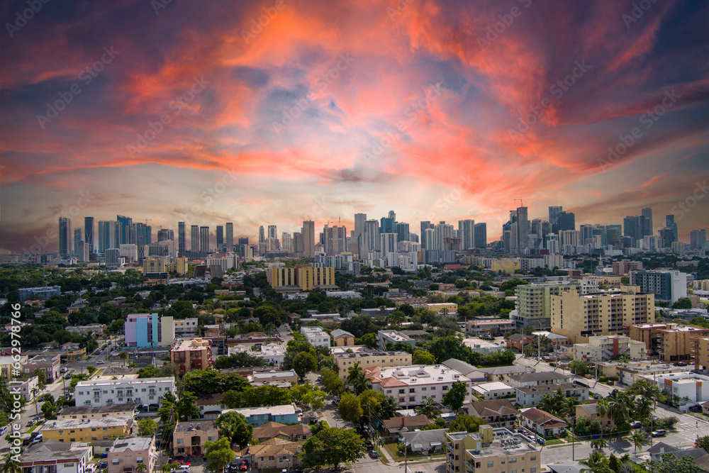 stunning aerial view with hotels, office buildings and skyscrapers in the city skyline, homes and apartments surrounded by lush green trees, cars on the street at sunset in Miami Florida USA