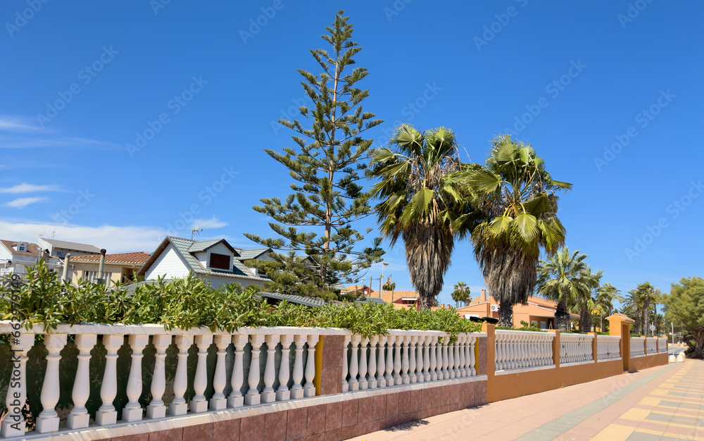 Fence with bushes and green garden at the villa. Exterior. Fence house at street with pavement road. Villa at seaside. Garden in luxury apartments. Fence and facade of house. House Exterior at coast.