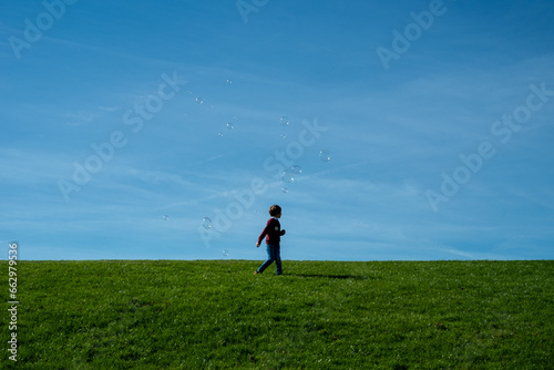 silhouette of a child on a hill playing with some soap bubbles in the sky