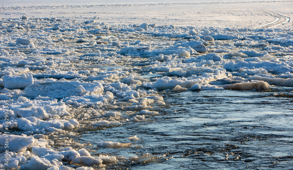 Thick white snow-covered ice floes float along the river. Spring ice drift. Thick white snow-covered ice floes float along the river. Spring ice drift.