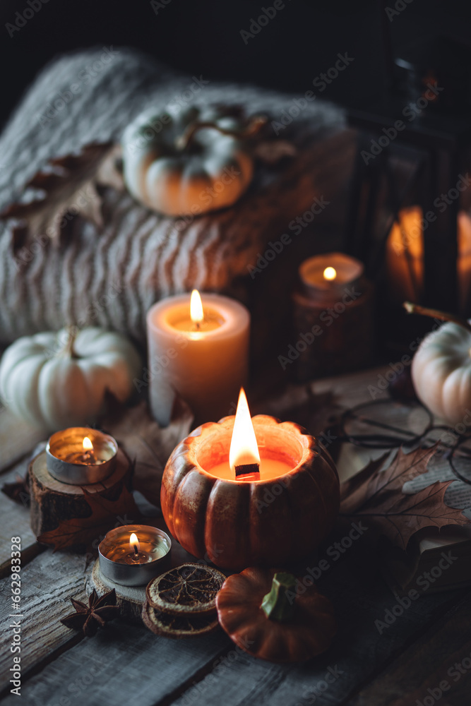 Cozy autumn home still life scene. Ceramic handmade pumpkin mug with burning candle near the window. Fall mood, Thanksgiving concept. Pumpkins, dry leaves, wool sweater, wooden background Cozy autumn home still life scene. Ceramic handmade pumpkin mug with burning candle near the window. Fall mood, Thanksgiving concept. Pumpkins, dry leaves, wool sweater, wooden background