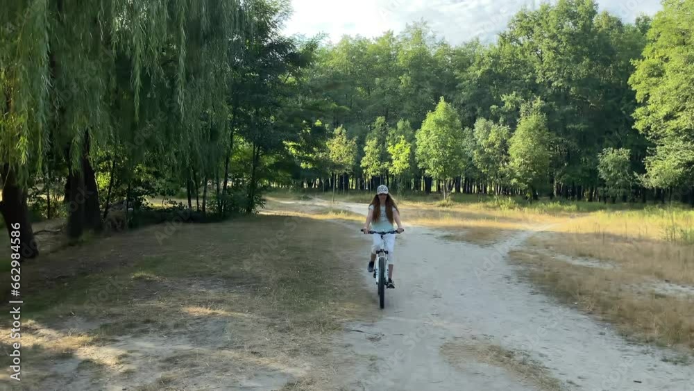 A young woman enjoys riding a bicycle in the park on the weekend. Attractive cyclist girl on vacation by the lake, leads an active lifestyle, enjoys a walk in the park and leisure time on vacation