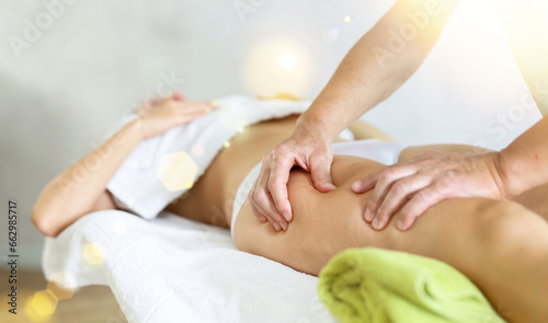 Hands of aged masseur massaging hip of female patient lying on massage table