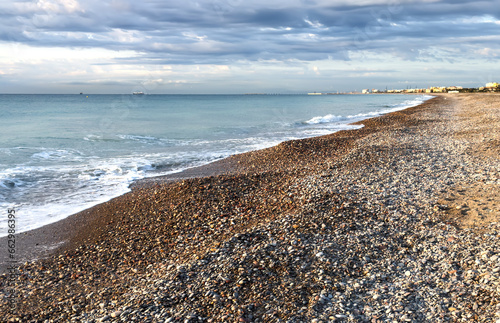 Pebble stone beach on sunrise. Sea beach landscape. Coastline on empty pebble beach on sunset. Coast pebbles. Shore landscape on Spain, Almarda resort. Ocean shoreline scenic. Waves in sea on sunrise. photo