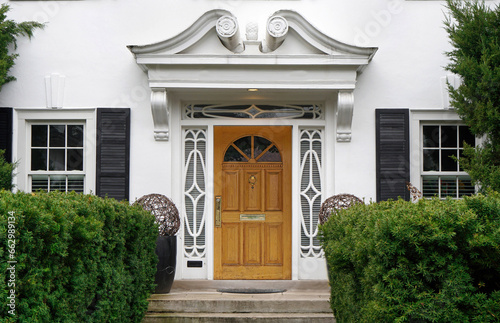 Photo Front door of white stucco house with shrubbery