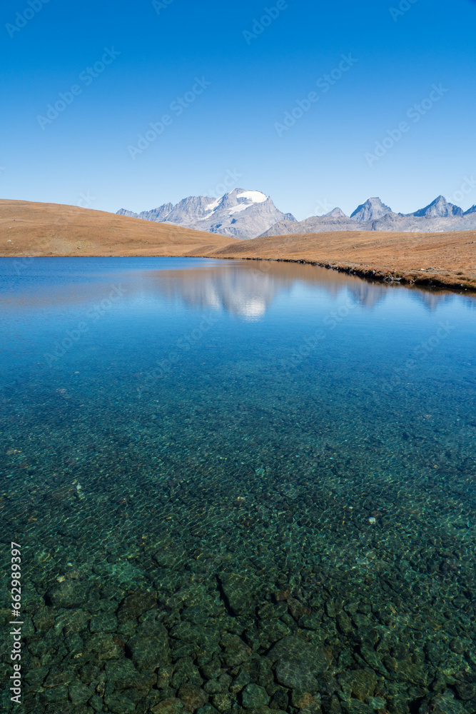 Rossett Lake with reflection, clear water and stones foreground, gran paradiso mountain with glacier background. national park landscape in autumn. Italian Alps