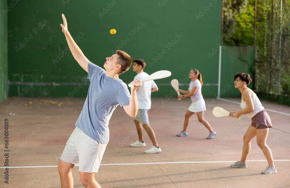 Young male pelota player hitting ball with wooden paleta during training game on outdoor Basque pelota fronton.