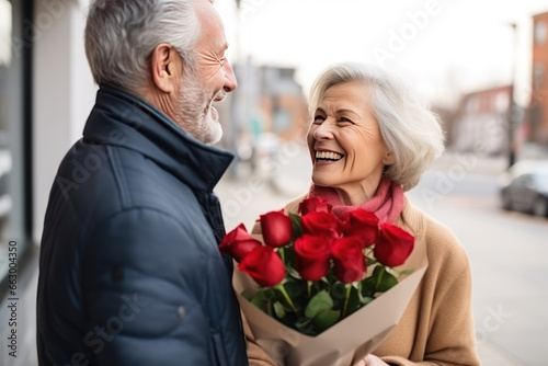 Elderly handsome man giving a bouquet of roses to a happy woman, present greeting, attention © Jam