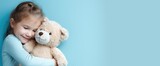 a girl hugging a teddy bear on a blue background with copy space