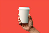 Paper coffee cup in hand, floating in the air, on flat plain background.