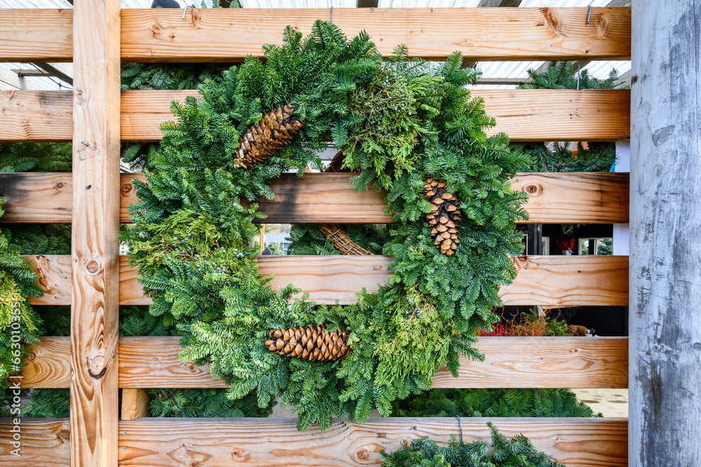 Fresh Christmas wreath made out of live evergreen branches and pine cones hanging on a rustic wood wall, Christmas holiday decoration
