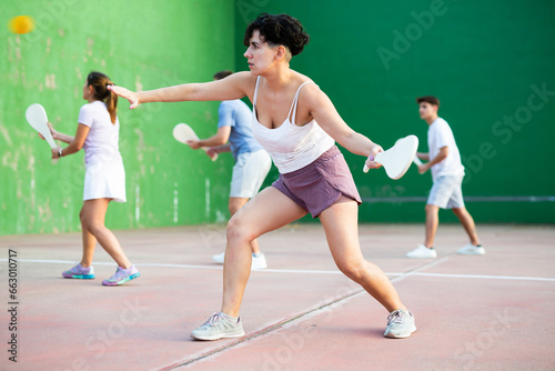 Portrait of sporty young girl playing paleta fronton on outdoor court, ready to hit ball. Healthy and active lifestyle concept