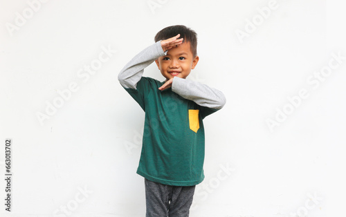 Curious boy wearing grey layered long sleeve green t-shirt standing while raised his hand to look something