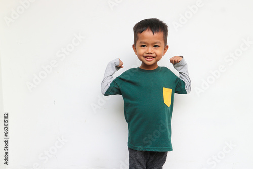 Happy smiling boy wearing layered long sleeve t-shirt standing and showing his strengths while raised his bicep muscle