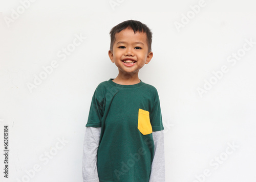 Happy smilling boy wearing layered long sleeve t-shirt standing and looking at camera. Isolated on grey background