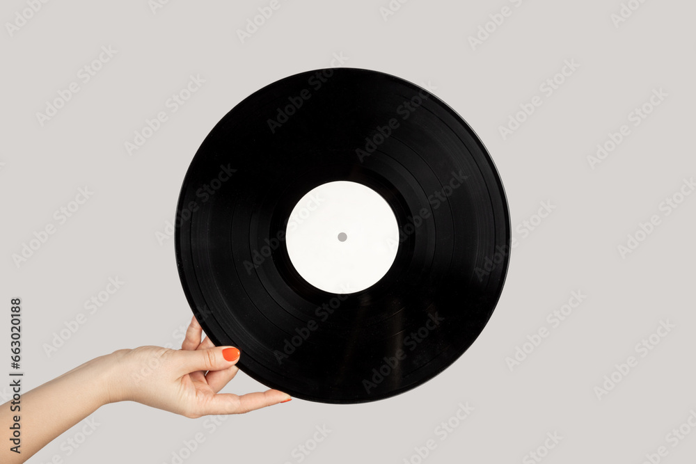 Fototapeta premium Closeup of woman hand showing retro spinning music plate for gramophone. Indoor studio shot isolated on gray background.