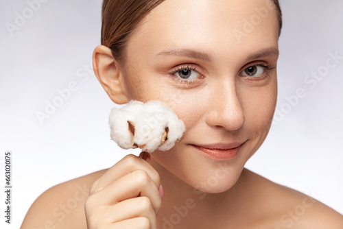 Closeup portrait of beautiful woman with well groomed perfect skin holding white flower lookingat camera, skincare concept. Indoor studio shot isolated over gray background. photo