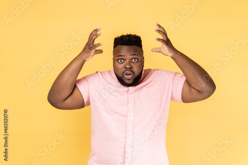 Portrait of astonished exhausted man wearing pink shirt showing explosion, looking worried and shocked, deadline, professional burnout. Indoor studio shot isolated on yellow background.