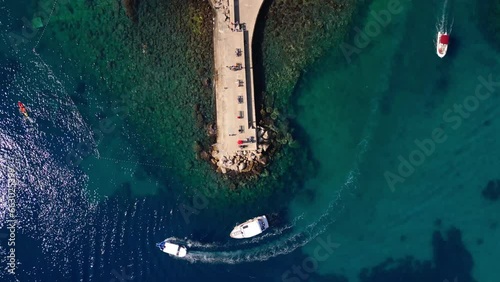 Bird's eye aerial shot of boats circling a pier in Dubrovnik, Croatia in the Adriatic sea during the day.