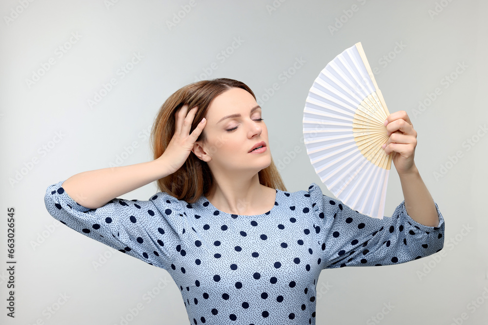 Beautiful woman waving hand fan to cool herself on light grey background Beautiful woman waving hand fan to cool herself on light grey background