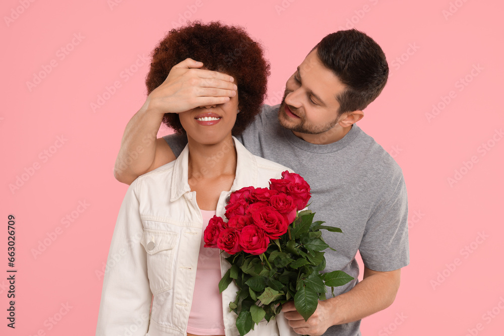 International dating. Handsome man presenting roses to his beloved woman on pink background International dating. Handsome man presenting roses to his beloved woman on pink background