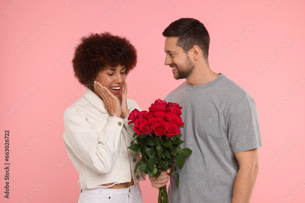 International dating. Handsome man presenting roses to his beloved woman on pink background International dating. Handsome man presenting roses to his beloved woman on pink background