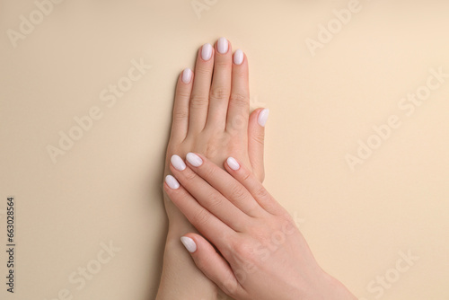 Woman showing her manicured hands with white nail polish on beige background, top view