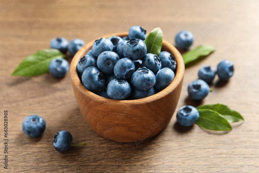 Bowl of tasty fresh blueberries with green leaves on wooden table, closeup Bowl of tasty fresh blueberries with green leaves on wooden table, closeup