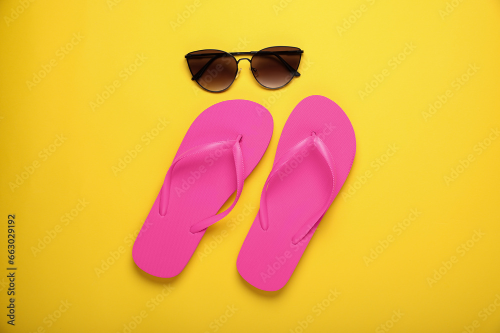 Stylish pink flip flops and sunglasses on yellow background, flat lay Stylish pink flip flops and sunglasses on yellow background, flat lay