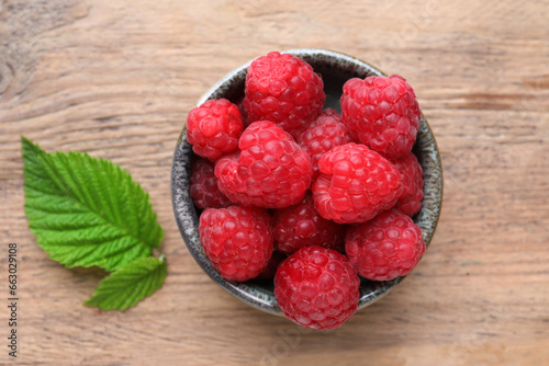 Tasty ripe raspberries and green leaves on wooden table, top view