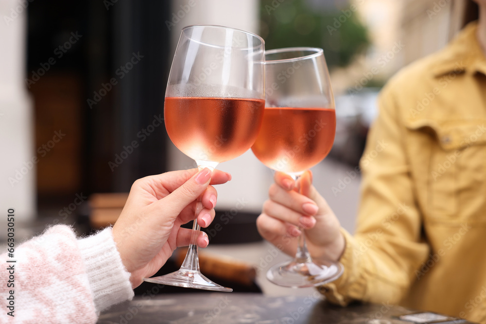 Women clinking glasses with rose wine at dark marble table in outdoor cafe, closeup Women clinking glasses with rose wine at dark marble table in outdoor cafe, closeup