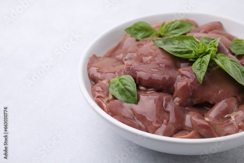 Bowl with raw chicken liver and basil on white table, closeup. Space for text